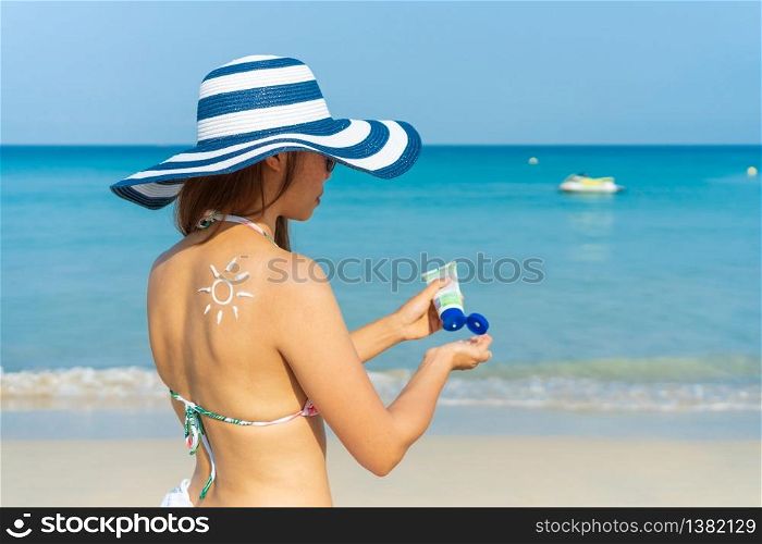 Young Asian woman with sun shape on the shoulder apply sun cream on to her hand. Summer on beach concept.
