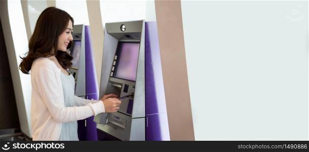 Young Asian woman withdrawing money with a card at the automatic machine, Female standing at ATM of the bank