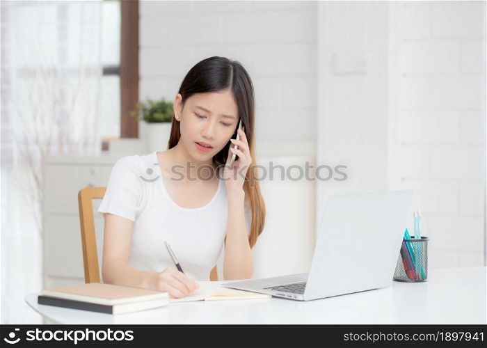 Young asian woman working on laptop computer and talking smartphone having stress and upset at home, girl having problem and worried, frustrated and unhappy, business and communication concept.