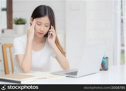 Young asian woman working on laptop computer and talking smartphone having stress and upset at home, girl having problem and worried, frustrated and unhappy, business and communication concept.