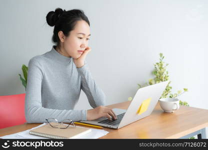 Young asian woman working on laptop in the home office desk, And sit at table resting chin on hand.