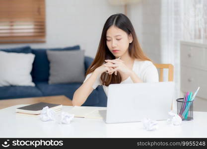 Young asian woman working with laptop computer think idea project and paper crumpled having problem on table at home, girl using notebook with frustrated and trouble, business and freelance concept.