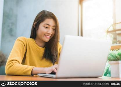 Young asian woman working with the laptop on a desk with her smi. Young asian woman working with the laptop on a desk with her smile. Young woman working on weekend with her laptop in a warm sunlight day. Laptop working in the house concept.