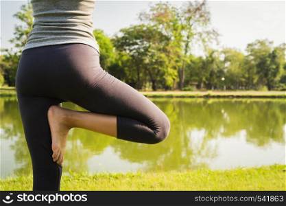 Young asian woman yoga outdoors keep calm and meditates while practicing yoga to explore the inner peace. Yoga have good benefits for health near lake at park. Sport and Healthy lifestyle concept.