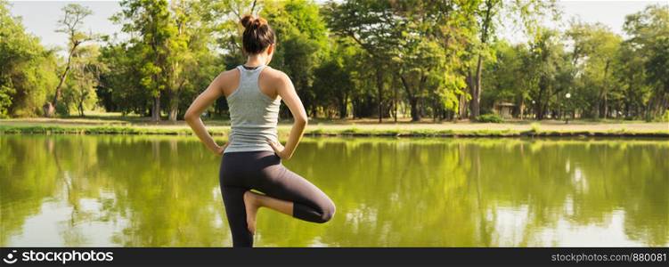 Young asian woman yoga outdoors keep calm and meditates while practicing yoga to explore the inner peace. Yoga have good benefits for health near lake at park. Panoramic banner background.