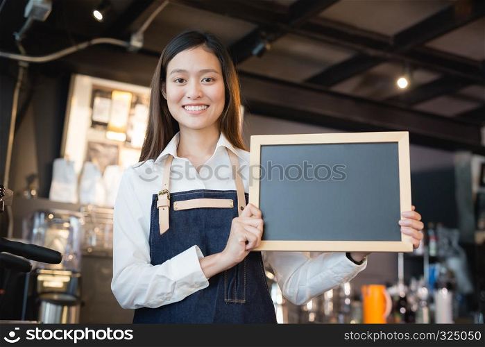 Young asian women barista holding blank chalkboard menu in coffee shop