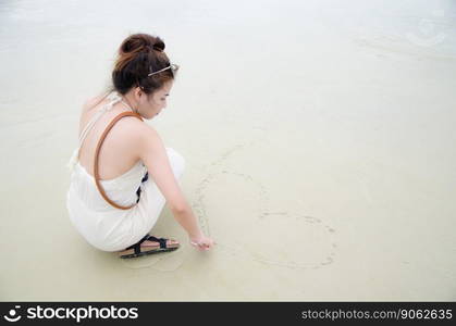 young asian women sitting on beach and drawing heart picture on sand