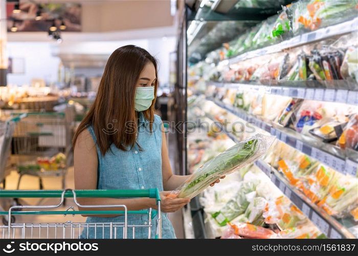Young asian women wearing surgical mask buying fresh vegetable in grocery store at supermarket during coronavirus outbreak, New normal lifestyle concept