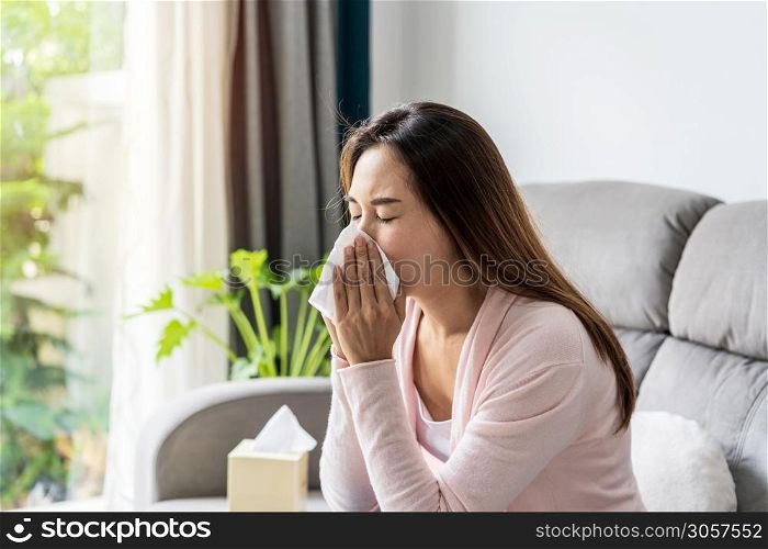 Young asian women with allergies feeling unwell using tissues and sneezing at home