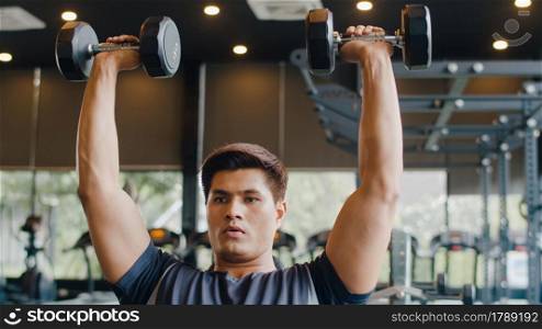 Young athlete Asian guy exercising doing lifting dumbbell fat burning workout in fitness class. Sportsman recreational activity, functional training, people working out, healthy lifestyle concept.