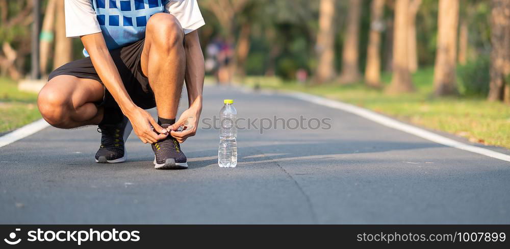Young athlete man tying running shoes in the park outdoor. male runner ready for jogging on the road outside. asian Fitness walking and exercise on footpath in morning. wellness and sport concepts
