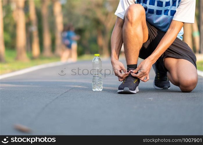 Young athlete man tying running shoes in the park outdoor. male runner ready for jogging on the road outside. asian Fitness walking and exercise on footpath in morning. wellness and sport concepts
