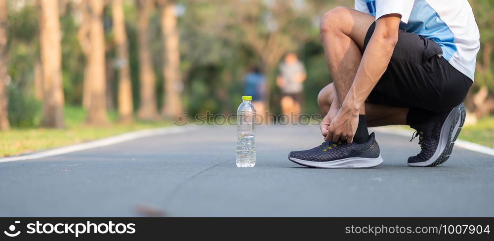 Young athlete man tying running shoes in the park outdoor. male runner ready for jogging on the road outside. asian Fitness walking and exercise on footpath in morning. wellness and sport concepts