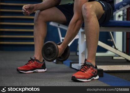 young athlete sitting on a bench and lifting weights in a gym
