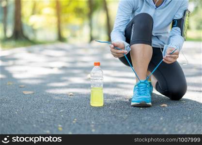 Young athlete woman tying running shoes in the park outdoor, female runner ready for jogging on the road outside, asian Fitness walking and exercise on footpath in morning. wellness and sport concepts