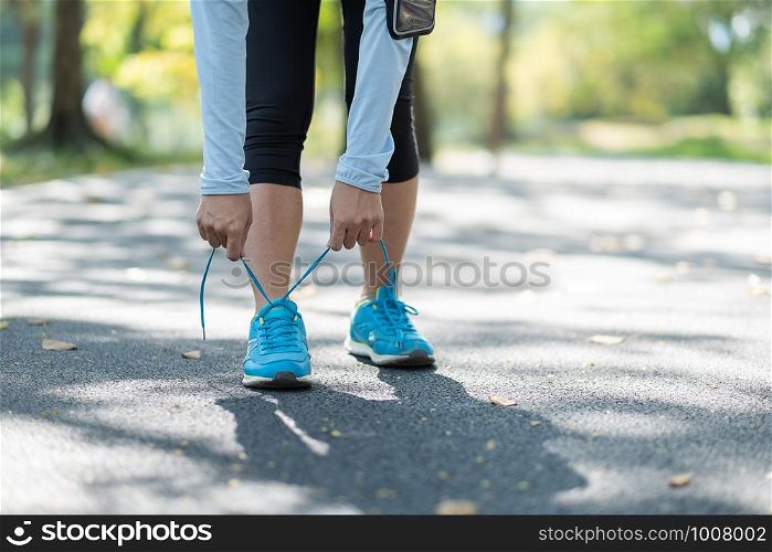 Young athlete woman tying running shoes in the park outdoor, female runner ready for jogging on the road outside, asian Fitness walking and exercise on footpath in morning. wellness and sport concepts