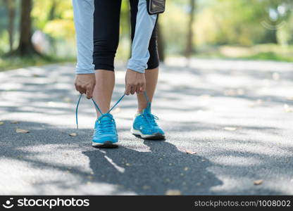 Young athlete woman tying running shoes in the park outdoor, female runner ready for jogging on the road outside, asian Fitness walking and exercise on footpath in morning. wellness and sport concepts