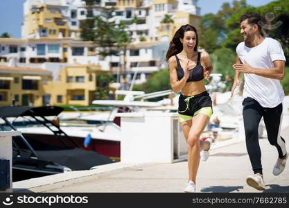 Young athletic couple training together running near the boats in a harbour. Young couple training together running near the boats in a harbour