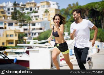 Young athletic couple training together running near the boats in a harbour. Young couple training together running near the boats in a harbour