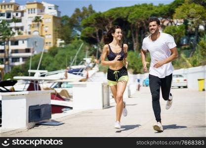 Young athletic couple training together running near the boats in a harbour. Young couple training together running near the boats in a harbour