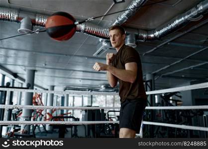 Young athletic man boxer strong fighter training with punching bag in gym ring preparing for training. Young boxer trains with punching bag in gym