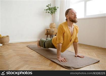 Young athletic man standing in Urdhva Mukha Svanasana yoga pose. Male sportive person practicing upward facing dog. Home training for health and body care. Young athletic man standing in Urdhva Mukha Svanasana yoga pose