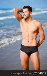 Young athletic man with fitness body standing on the sand of the beach. Young athletic man with fitness body standing on the beach