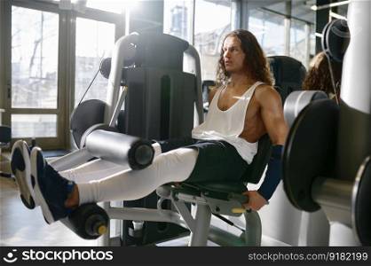 Young athletic sportsman pumping muscle exercising and flexing legs on gym machine. Sport club interior on background. Sportsman pumping muscle exercising and flexing legs on gym machine