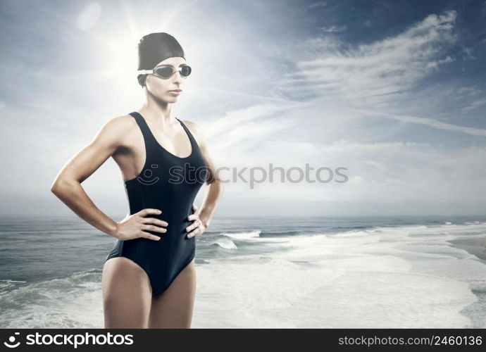 Young athletic swimer woman with googles and swimming cap, with the beach as background