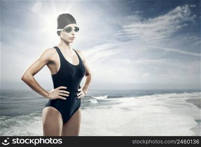 Young athletic swimer woman with googles and swimming cap, with the beach as background