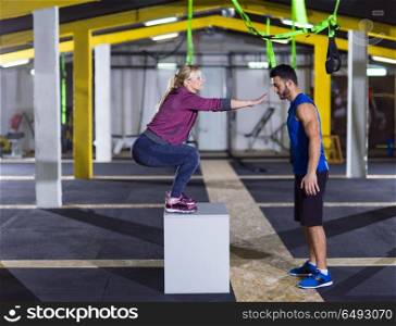 young athletic woman training with personal trainer jumping on fit box at crossfitness gym. woman working out with personal trainer jumping on fit box