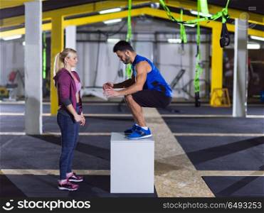 young athletic woman training with personal trainer jumping on fit box at crossfitness gym. woman working out with personal trainer jumping on fit box
