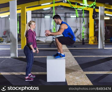 young athletic woman training with personal trainer jumping on fit box at crossfitness gym. woman working out with personal trainer jumping on fit box