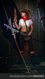 Young attractive armed girl pirate captain looks into the distance on the background of the flag Jolly Roger. Girl Pirate Captain