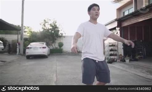 Young attractive asian man in casual dress stretching body before exercising at village street, warming body up before exercise by raising hands up together, sunlight in background, healthy leisure