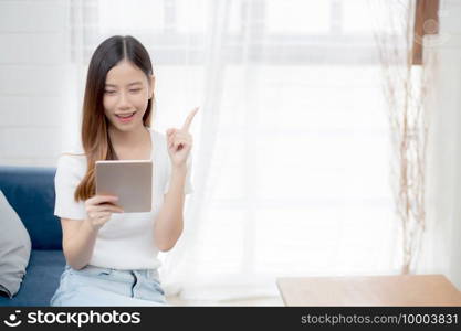 Young attractive asian woman resting using browsing tablet computer on sofa at home, happy girl sitting on couch relax looking digital gadget with excited, communication and lifestyle concept.