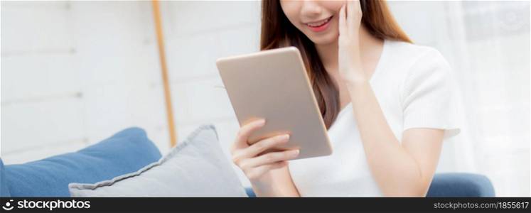 Young attractive asian woman resting using browsing tablet computer on sofa at home, happy girl sitting on couch relax reading digital gadget at house, communication and lifestyle concept.
