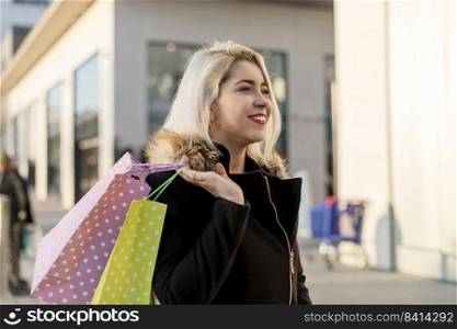 Young attractive blonde woman in a black jacket against the backdrop of the city streets. Holding a lot of shopping bags.