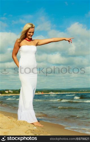 Young attractive blonde woman pointing showing sky. Portrait of gorgeous girl wearing white dress in summer time.. Beauty blonde woman pointing to sky.