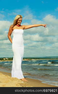 Young attractive blonde woman pointing showing sky. Portrait of gorgeous girl wearing white dress in summer time.. Beauty blonde woman pointing to sky.