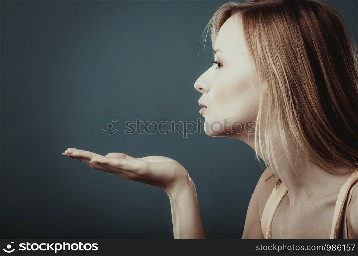 Young attractive blonde young woman sending hand kiss. Studio shot on gray blue background.
