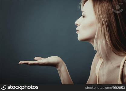 Young attractive blonde young woman sending hand kiss. Studio shot on gray blue background.