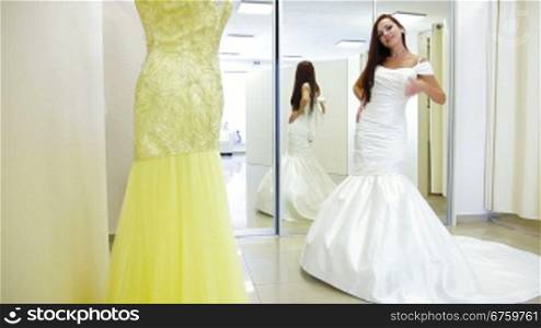 Young attractive bride trying on wedding dress in bridal shop, posing and looking at camera