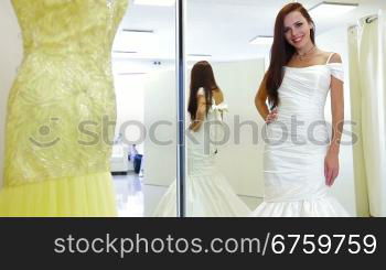 Young attractive bride trying on wedding gown in bridal shop, posing and looking at camera