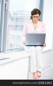 Young attractive business woman working on laptop computer in fron front of office window.