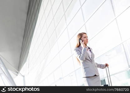 Young attractive businesswoman talking on smartphone while walking with her suitcase in airport