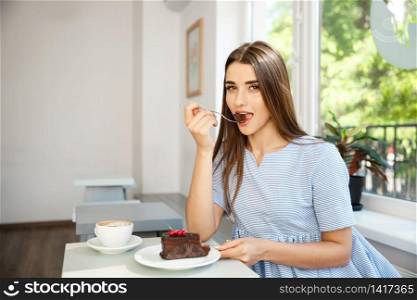 Young attractive Caucasian lady enjoy eating chocolate cake with hot coffee in modern coffee shop at noon.