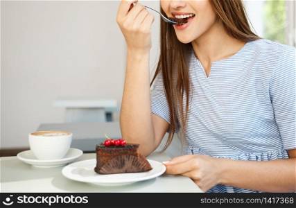 Young attractive Caucasian lady enjoy eating chocolate cake with hot coffee in modern coffee shop at noon.