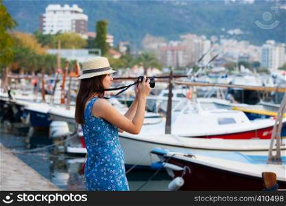 Young attractive cheerful travel girl walking with camera in old Mediterranean city seafront. Summer resort travel concept. Young attractive cheerful travel girl walking with camera