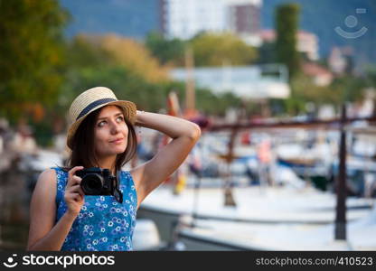 Young attractive cheerful travel girl walking with camera in old Mediterranean city seafront. Summer resort travel concept. Young attractive cheerful travel girl walking with camera